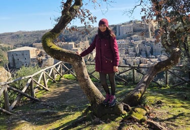 Donna sorridente in un prato di montagna appoggiata a un albero