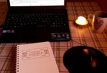 tavola con sopra agenda, computer che ostra programma di registrazione, lampada con luce soffusa e tazza di tisana