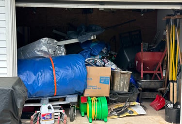 Cluttered garage storage space filled with boxes, garden tools, and a blue tarp needing organization.