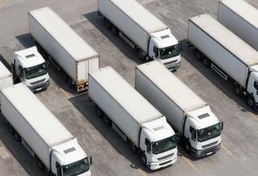 A bird's eye view of several white trucks parked in an organized grid at a terminal. Clean, sharp lines, professional and efficient atmosphere.