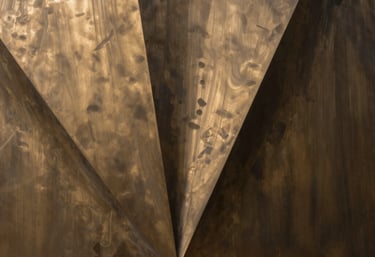 Abstract photography of light and shadows on a bronze metal surface, representing creative flair and corporate precision.