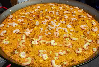 A large metal pan of authentic Spanish seafood paella with yellow rice and fresh pink shrimp.