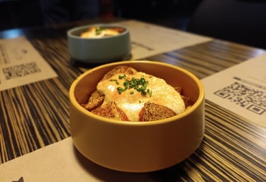 Crispy patatas bravas topped with creamy aioli and fresh chives in a yellow ceramic bowl.