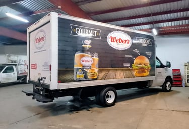 A Weber's Bread delivery truck parked in a warehouse featuring gourmet brioche bun advertisements.