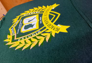 Custom screen printed yellow school crest logo on a dark green cotton t-shirt fabric.