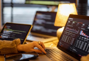 A software developer analyzes data charts and code on multiple laptop screens in a warm home office.