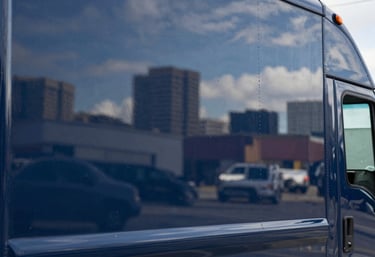 A close-up of a polished navy blue delivery truck's side panel. The surface is clean and reflects a North American / US city skyline, representing professional service.