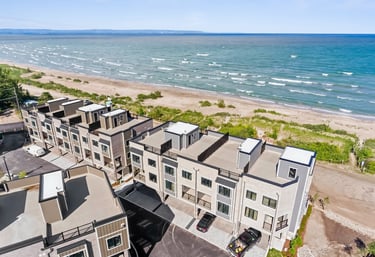 Aerial view of modern luxury beachfront townhomes with rooftop patios overlooking a sandy beach and blue waves.