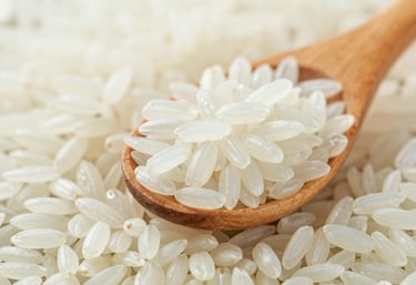Macro shot of polished Jasmine rice grains held in a wooden scoop, showcasing their long-grain structure and pure white color. Lighting is clean and natural, consistent with #F5F6F3.