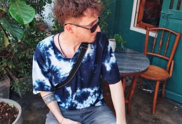 In a blue tie-dye shirt and sunglasses Unicris sitting at an outdoor cafe with plants.