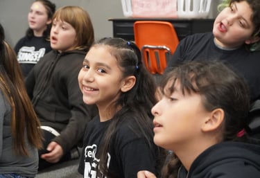 Smiling young girl participating in a group school activity with classmates in a classroom setting.