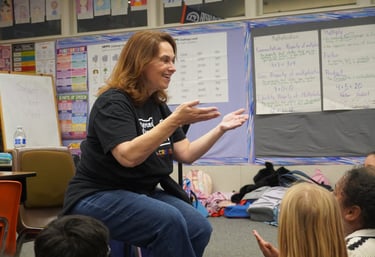 A smiling music teacher gestures while teaching a classroom lesson to students.