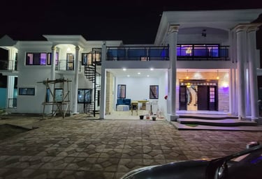 Luxury white two-story modern house illuminated at night with a spiral staircase and stone driveway.
