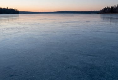 A serene, minimalist image of a calm frozen lake at dawn in North America, with subtle ripples and a soft ice blue and charcoal color palette. Evokes a sense of order and calm.
