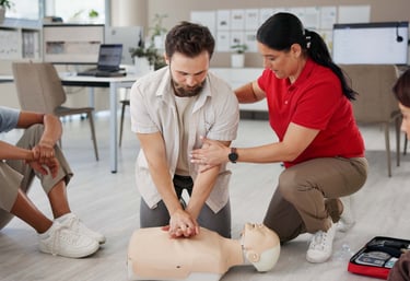 Female instructor assisting a male student learning how to perform CPR on a training mannequin