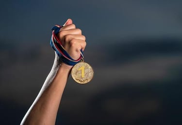 Atleta com o braço ergudi segurando uma medalha de ouro com 1º lugar