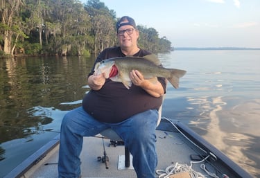 Paul sitting in boat holding a Large Mouth Bass