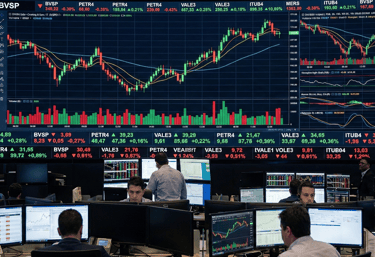 Um grupo de pessoas está sentado em mesas com vários monitores. analisando o mercado de ações