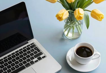 A modern flat-lay of a laptop, a cup of coffee, and a fresh vase of tulips on a clean, soft-blue desk surface, high-key lighting, North American office.