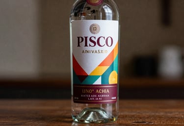 A custom Pisco bottle with a modern, colorful anniversary label featuring deep burgundy accents, photographed in a high-end South American / Peruvian setting.