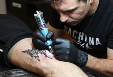 Close-up of a tattoo artist working meticulously on a client's skin in a neon-lit studio.