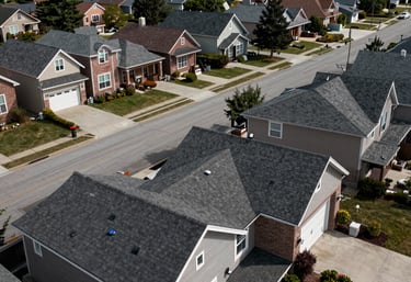 Wide-angle photograph of a street in a North American suburb showcasing several houses with perfectly maintained, expert roofing. The atmosphere is quiet and professional.