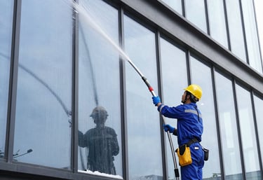 A professional technician pressure washing a commercial storefront on a sunny day.