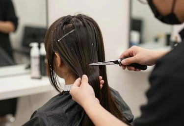 A stylist carefully trimming a woman's hair in a softly lit salon with pastel pink accents.