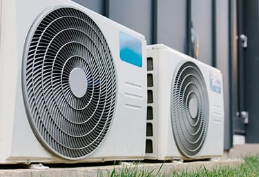 Two modern air conditioning compressor units installed outside a residential home for efficient HVAC cooling.