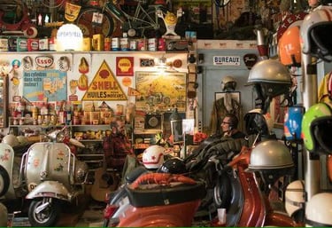 Vintage scooter repair shop filled with classic Vespas, retro helmets, and antique oil signage.