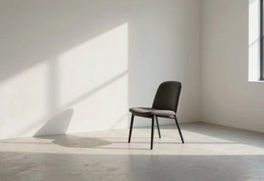 Photography of a modern interior featuring a single charcoal chair in a large off-white room with generous negative space and dramatic shadows.