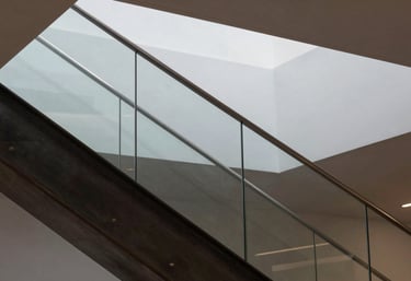A close-up of a modern, minimal architectural staircase made of dark steel and glass. High-contrast lighting. Global / High-end corporate.