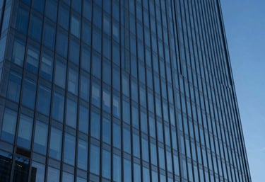 A professional photography shot of a sleek glass skyscraper reflecting a deep blue evening sky. Sharp lines, minimalist composition. Global / High-end corporate.
