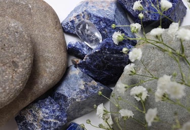 “Sodalita azul con piedras de río y flores blancas delicadas.”