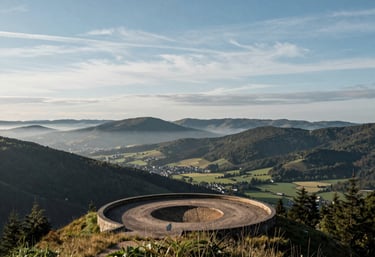 A scenic overlook from the top of the bike park showing the valley of Remiremont under a blue sky with soft clouds, misty green mountains, French / Vosges Region.