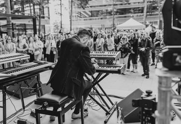 Nuotrauka iš įmonės renginio. Ant scenos groja pianistas. Prie scenos susirinkusi didelė publika.