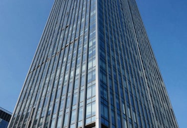 A low-angle shot of a stunning modern glass skyscraper reflecting a royal blue sky. The image emphasizes structural engineering excellence and grand scale. Clean, crisp architectural style.