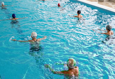 A group of joyful seniors participating in a swimming session, guided by a friendly coach in a bright indoor pool.