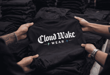 Manos sosteniendo una playera de la marca Cloud Wake Wear