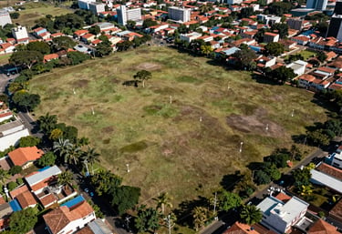 Overhead aerial-style shot of a flat land plot in a Brazilian urban fringe, clear boundary markers visible, surrounding neighborhood context, daylight