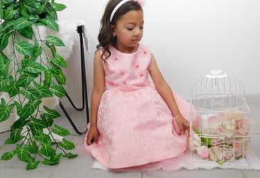 Niña con vestido de fiesta floral en tonos rosa, sentada junto a una jaula blanca decorada