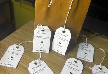 Personalized wedding favor tags with names Thais and Fernando next to a gold gift bag.