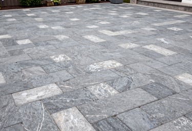 Wide shot of a luxury outdoor patio in a North American / US backyard featuring interlocking paving stones in shades of slate grey and pale cloud.