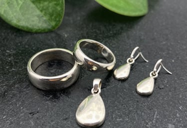 Close-up of handcrafted silver jewelry pieces arranged on a soft jade green fabric.
