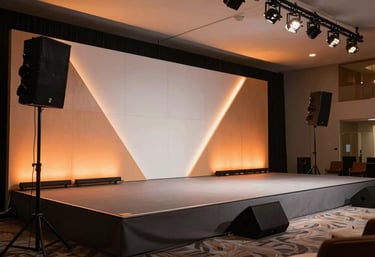 A sleek, modern corporate stage setup in a Latin American business center. The design features geometric panels illuminated with burnt orange lights and professional audiovisual equipment.