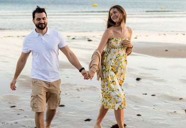 Couple holding hands, walking barefoot along a golden Algarve beach, smiling
