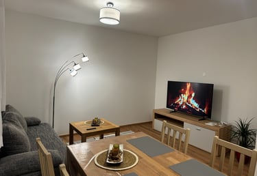 Modern living room with a fireplace video on the TV, arc floor lamp, and a wooden dining table.