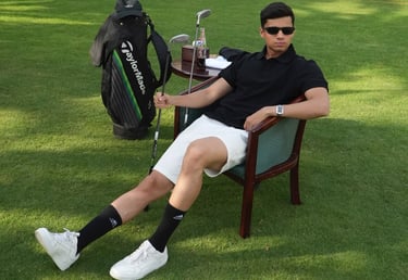 A young man wearing a polo shirt and sunglasses relaxes on a golf course with a TaylorMade golf bag and clubs.