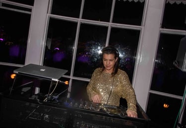 Female DJ in a gold sequin top performing a live set with a mixer and laptop at a night event.