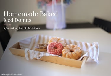 Homemade baked iced donuts with pink sprinkles on a wooden tray with a kitchen towel.